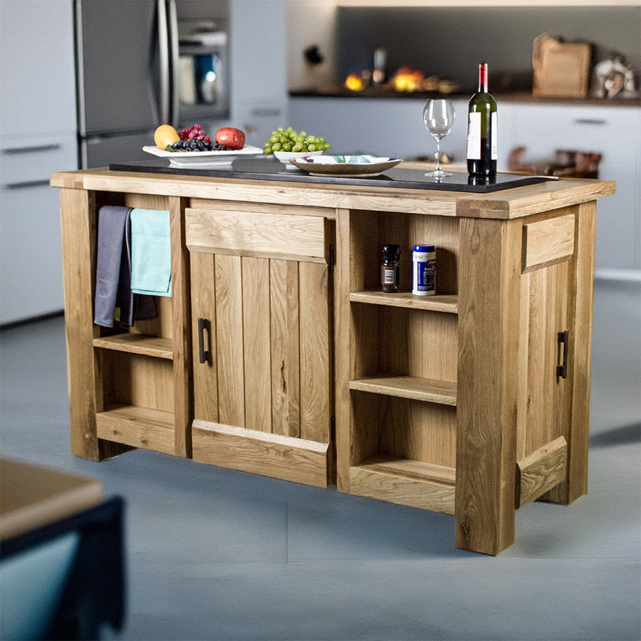 An overall view of the Camden Granite Top Kitchen Workbench. There is a bottle of wine, a wine glass, a plate and two platters of fruit on top. There are two hand towels on the towel rail, and a salt and pepper shaker on the top shelf on the right.