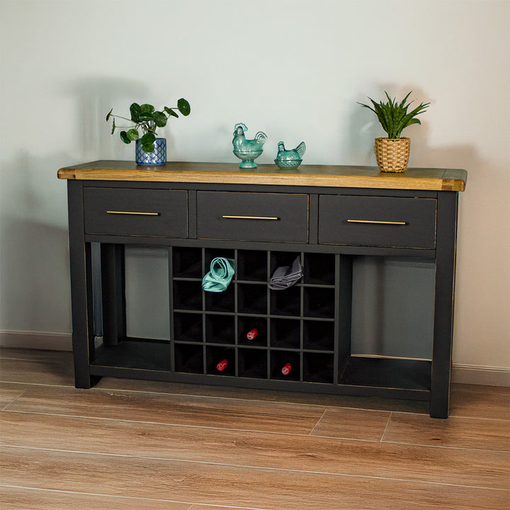 The front of the Cascais Large Buffet with Wine Rack. There are two small potted plants on top in between two blue glass ornaments. There are three wine bottles in the wine rack and two towels in the top.