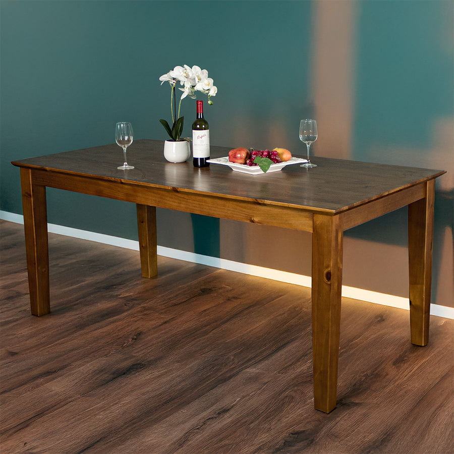 The front of the Hamilton Dining Table with Rimu Finish (1.8m). There are two wine glasses, a pot of white flowers, a fruit platter and a bottle on top of the table.
