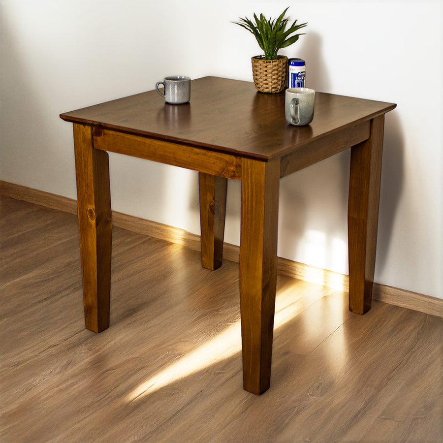 The front of the Hamilton Pine Dining Table (800mm). There is a potted plant, two mugs and a salt shaker on top.
