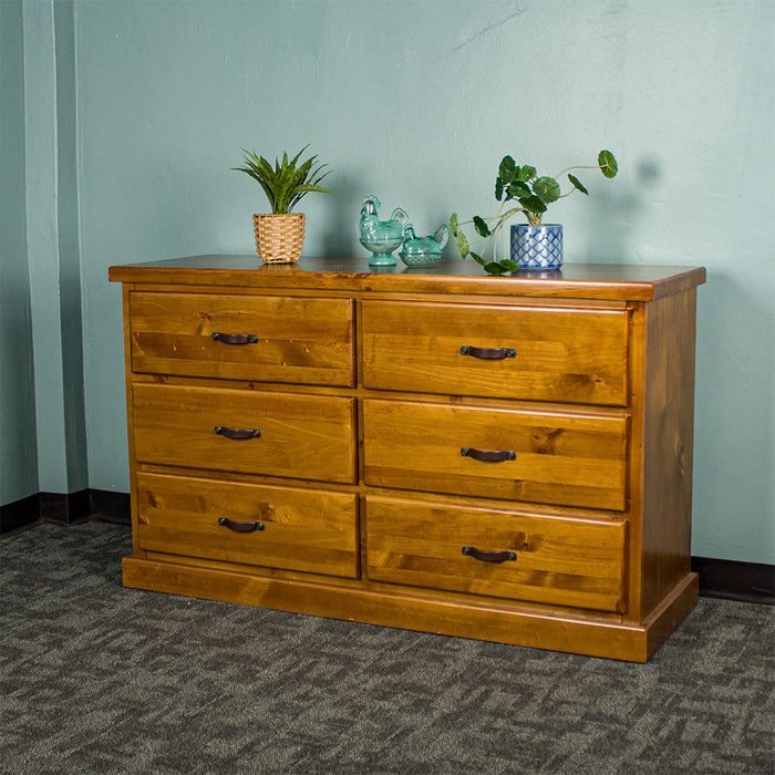 Front view of the Jamaica 6 Drawer Pine Lowboy, there are two potted plants and two blue glass ornaments on top.