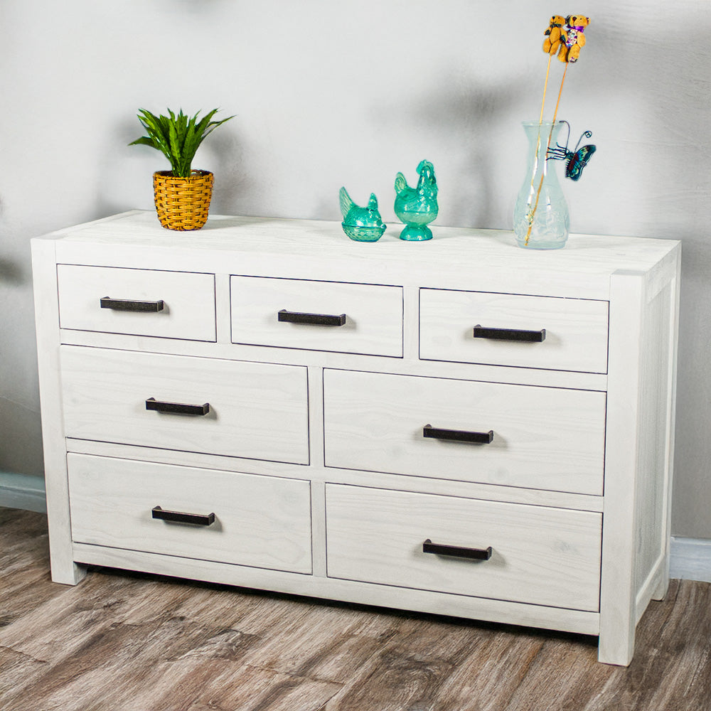 The front of the Vancouver 7 Drawer White Lowboy. There is a potted plant and three blue glass ornaments on top.