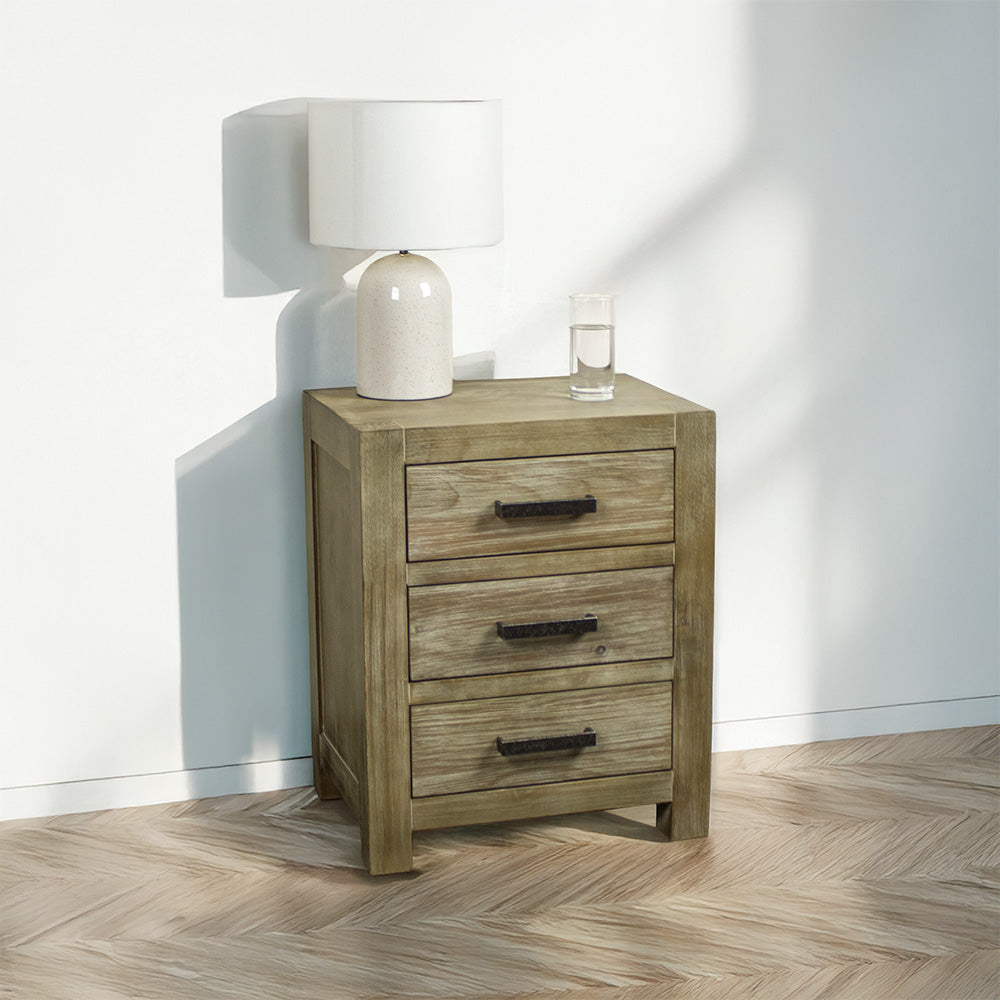 The front of the stonewash Vancouver 3 Drawer Bedside Cabinet. There is a lamp and a glass of water on top.