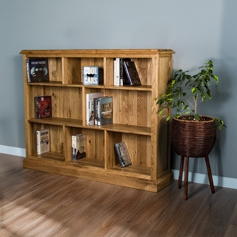 The front of the Versailles Outback Oak Three Level Bookcase. There are various books on each of the shelves, and a free standing potted plant next to the bookshelf.