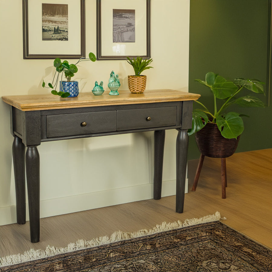 An overall view of the Boston Oak Hall Table - Black. There are two potted plants on top of the table, with two blue glass ornaments in between. There is a free standing potted plant next to the table.
