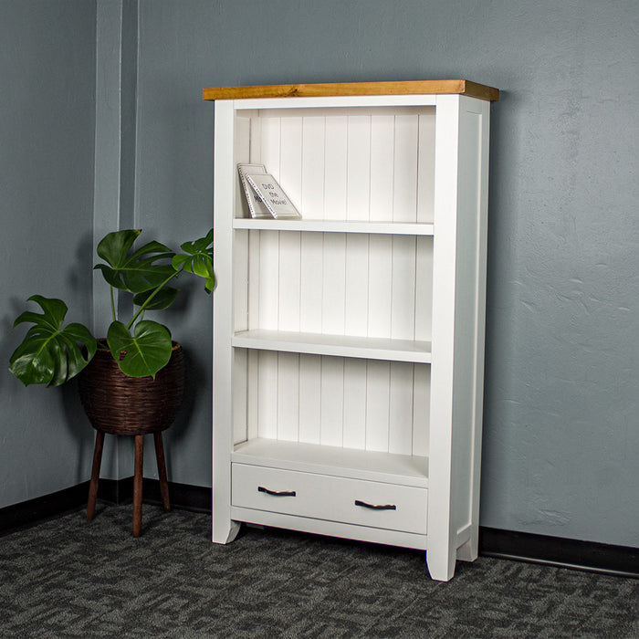 The front of the Felixstowe Pine Bookcase. There are two DVDs on the top shelf. There is a free standing potted plant next to the bookshelf.