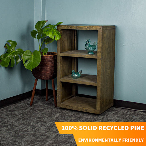 The Stonemill Recycled Pine Cube Shelf, with three shelves. There are two blue glass ornaments, one on the middle and one on the top shelf. There is a tall free standing potted plant next to the cube shelf.