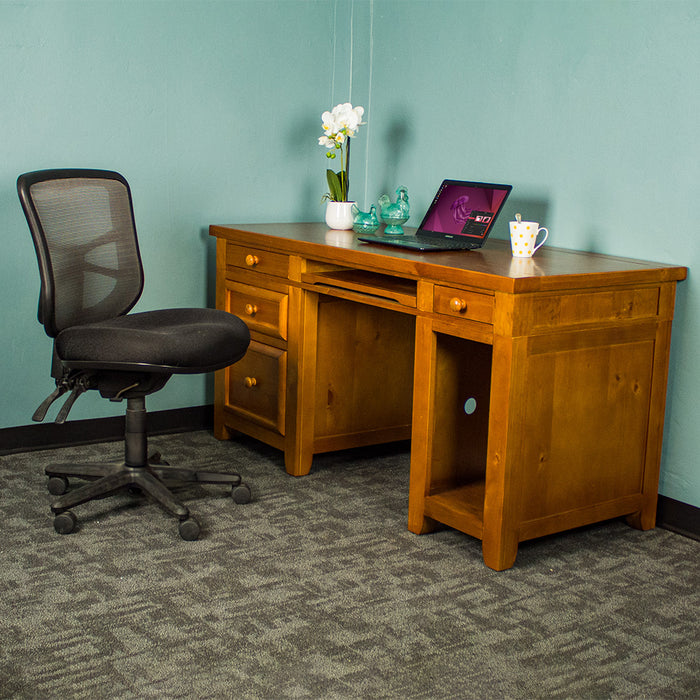 The front of the Cranford Computer Desk with Rimu Finish. There is an office chair in front. There is a small pot of white flowers, two blue glass ornaments, a laptop and a white coffee mug on top.