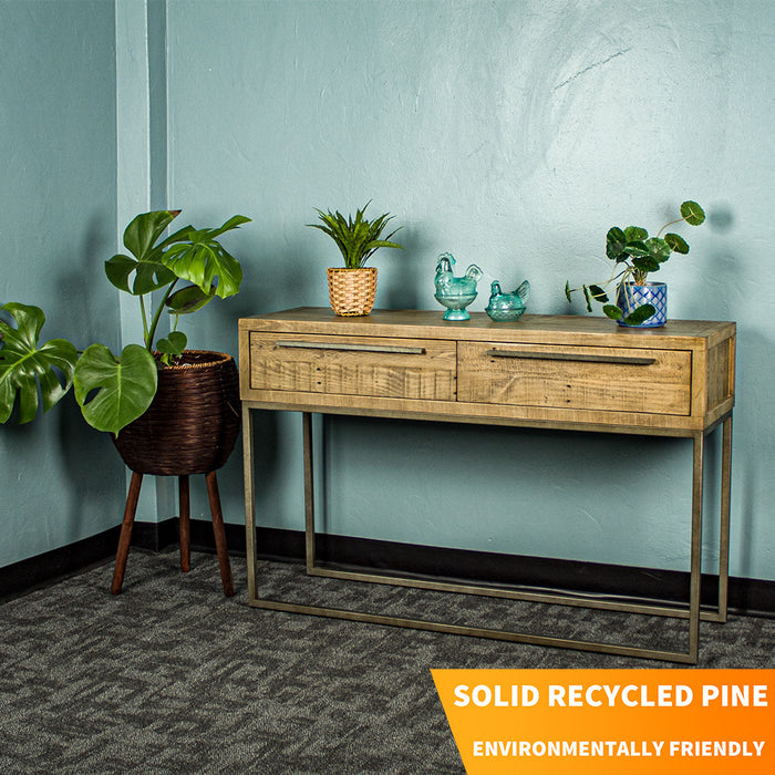 The front of the Monterey Recycled Pine Hall Table. There are two potted plants on top with two blue glass ornaments in the middle. There is a free standing potted plant next to it.