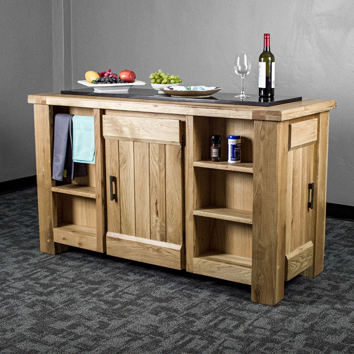 An overall view of the Camden Granite Top Kitchen Workbench. There is a bottle of wine, a wine glass, a plate and two platters of fruit on top. There are two hand towels on the towel rail, and a salt and pepper shaker on the top shelf on the right.