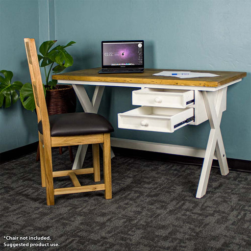 The front of the Byron Recycled Pine Desk with its drawers open. There is a laptop and a pile of paper on top of the desk. There is an upholstered oak dining chair in front of the desk and a free standing potted plant next to it.
