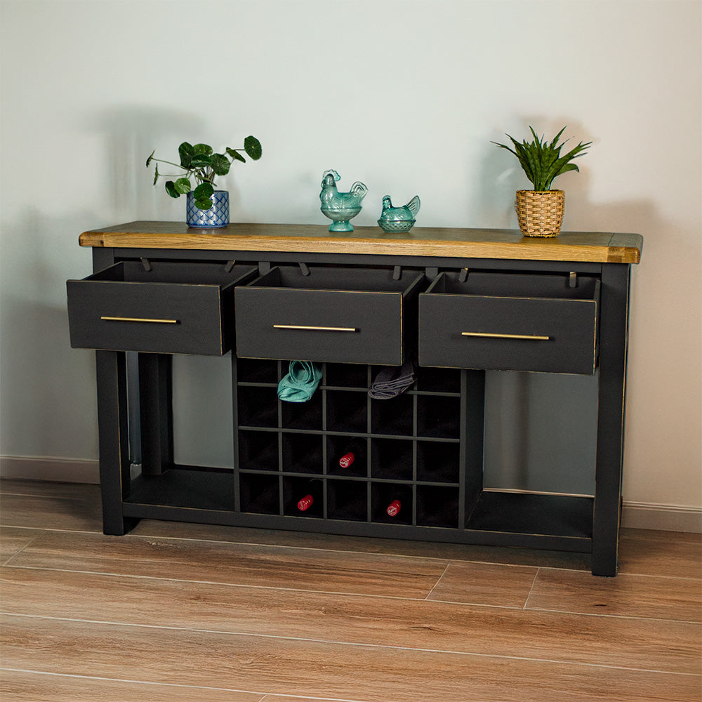 The front of the Cascais Large Buffet with Wine Rack with its drawers open. There are two small potted plants on top in between two blue glass ornaments. There are three wine bottles in the wine rack and two towels in the top.