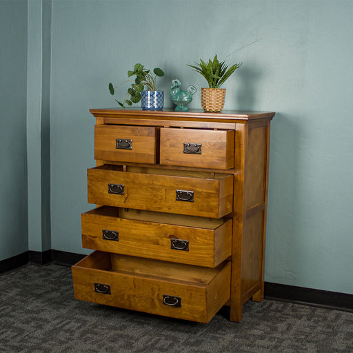 The front of the Montreal Five Drawer Pine Tallboy with its drawers open. There are two potted plants on top and a blue glass ornament in between.