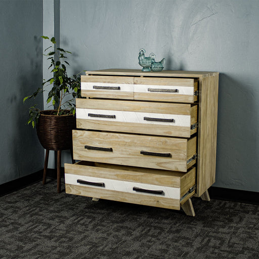 The front of the Soho 5 Drawer Tallboy with its drawers open. There are two blue glass ornaments on top with a free standing potted plant next to it.
