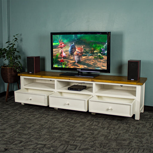 The front of the Tuscan Recycled Pine TV Unit with its drawers open. There is a DVD player in the middle shelf. There is a TV on top with two speakers on either side, and a free standing potted plant next to the TV stand.