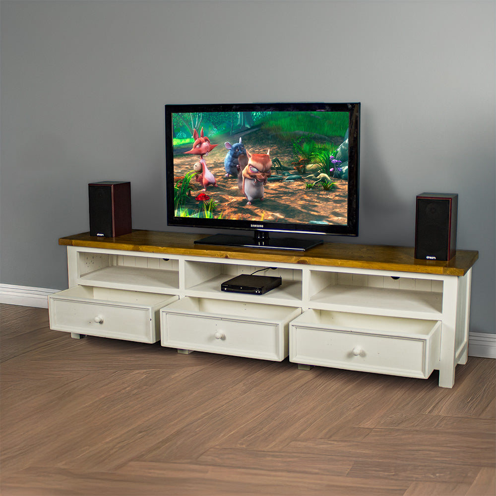 The front of the Tuscan Recycled Pine TV Unit with its drawers open. There is a DVD player in the middle shelf. There is a TV on top with two speakers on either side, and a free standing potted plant next to the TV stand.