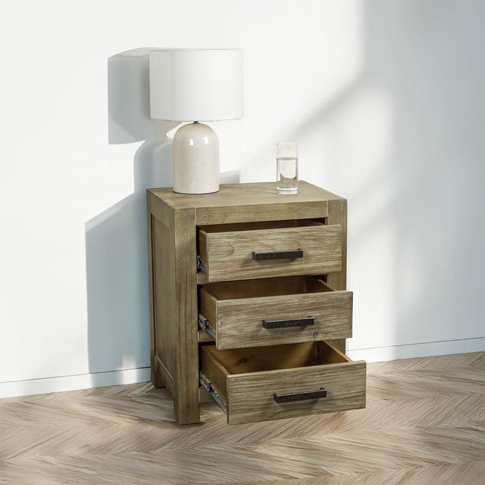 The front of the stonewash Vancouver 3 Drawer Bedside Cabinet with its drawers open. There is a lamp and a glass of water on top.
