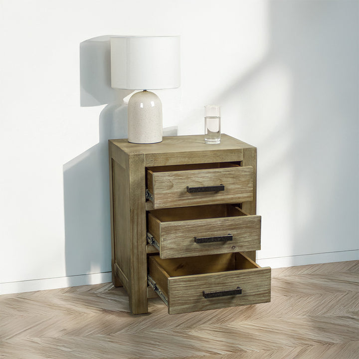 The front of the stonewash Vancouver 3 Drawer Bedside Cabinet with its drawers open. There is a lamp and a glass of water on top.