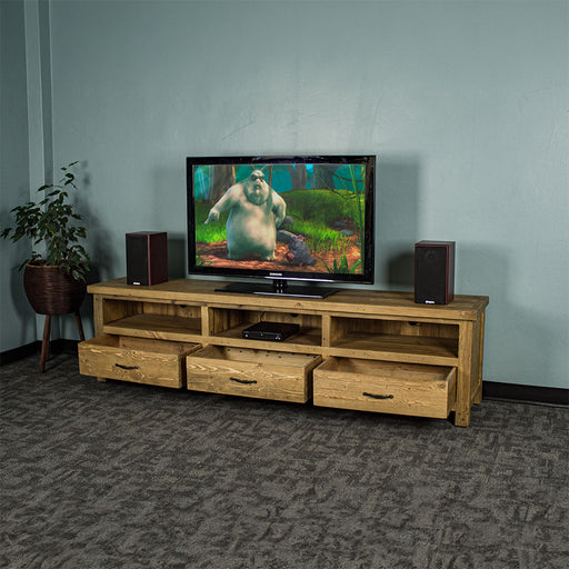 The front of the Ventura Recycled Pine Large TV Unit with its drawers open. There are two speakers on either side of a large TV in the middle on top of the unit. There is a DVD player in the middle shelf. There is a free standing tall potted plant next to the unit.