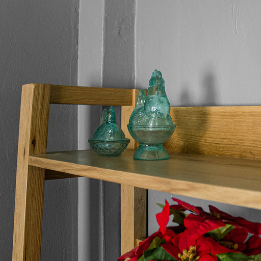 A close up of the top shelf on the Kubic Oak Display Shelf, there are two blue glass ornaments in the shape of chickens on the shelf.