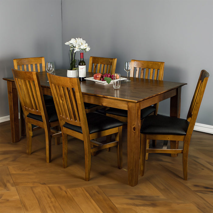 An overall view of the Hamilton 7 Piece Dining Suite with 1.5m Table. There are 6 Hamilton Rimu Stained Dining Chairs surrounding the table. There are four glasses on top, a pot of white flowers, a fruit platter and a bottle of wine on the top of the table.