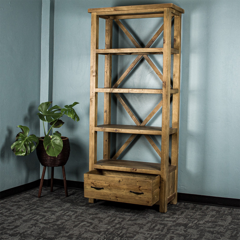The light brown Ventura Recycled Pine Bookcase with its drawer open, and a standing potted plant next to it.