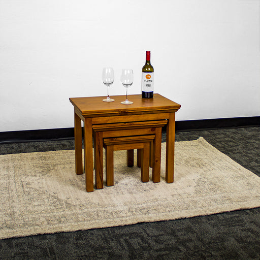 The Montreal 3 Piece Pine Nesting Tables on top of a cream coloured rug. There are two wine glasses and a bottle of wine on top.
