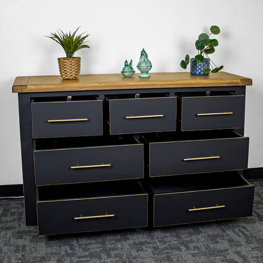 The front of the Cascais Oak Top 7 Drawer Lowboy (Black) with its drawers open. There are two blue glass ornaments in the middle on top with two potted plants on either side.