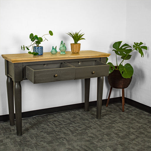 An overall view of the Boston Oak Hall Table - Black with its drawers open. There are two potted plants on top with two blue glass ornaments in between. There is a free standing potted plant next to the table.