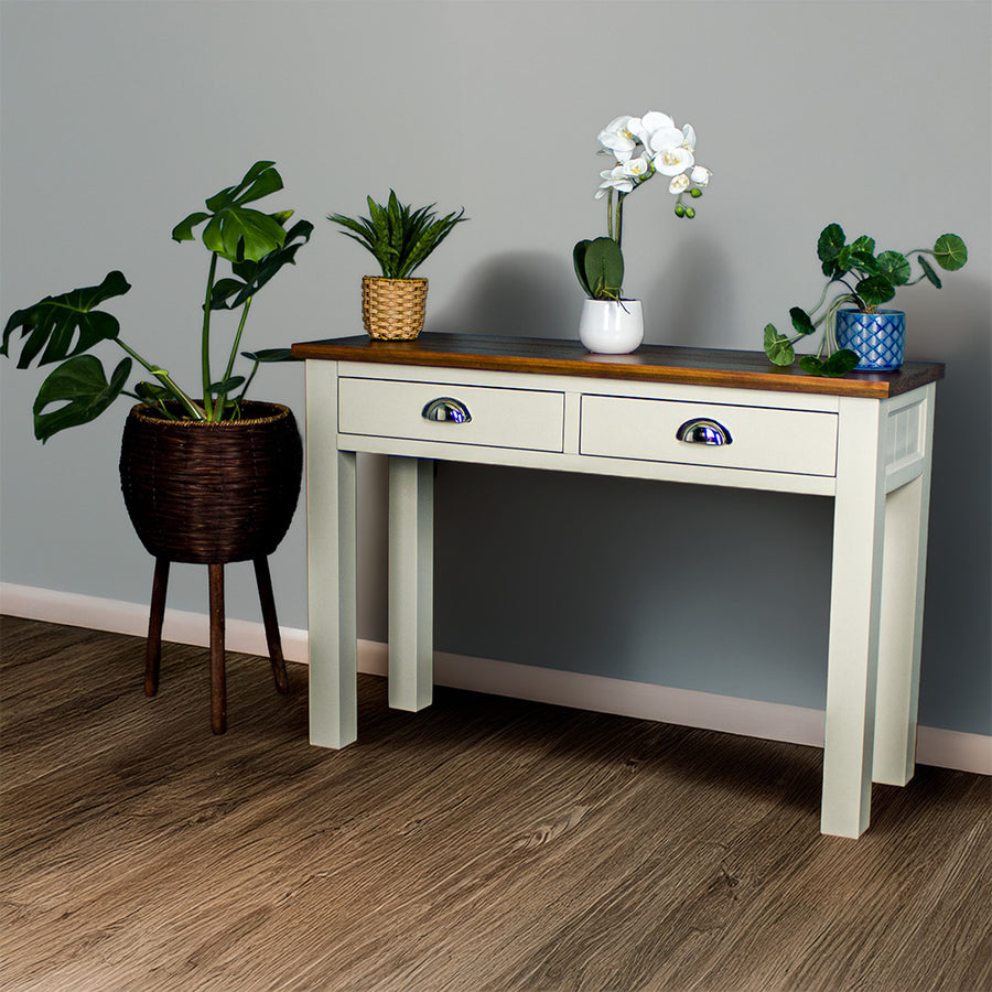 White Alton 2 Drawer Pine Hall Table with a rimu stained top. There are two potted plants on the top and a bouquet of flowers in the middle.