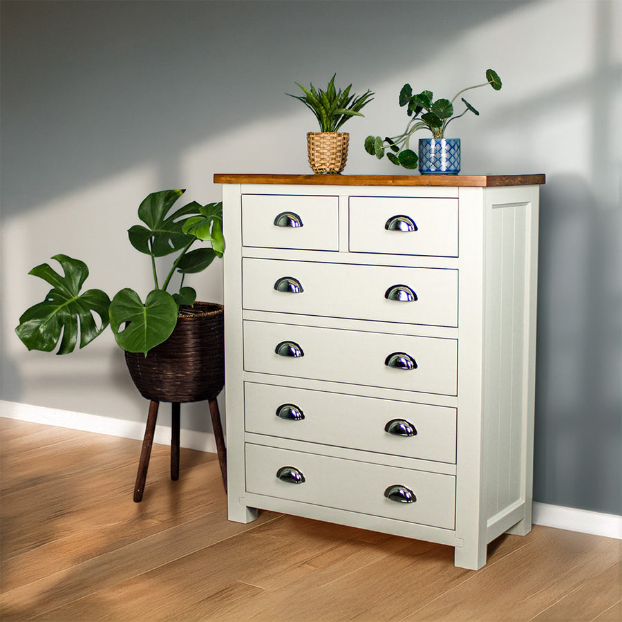 An overall view of the Alton 6 Drawer NZ Pine Tallboy. There is a free standing potted plant next to it. There are two potted plants on the top.