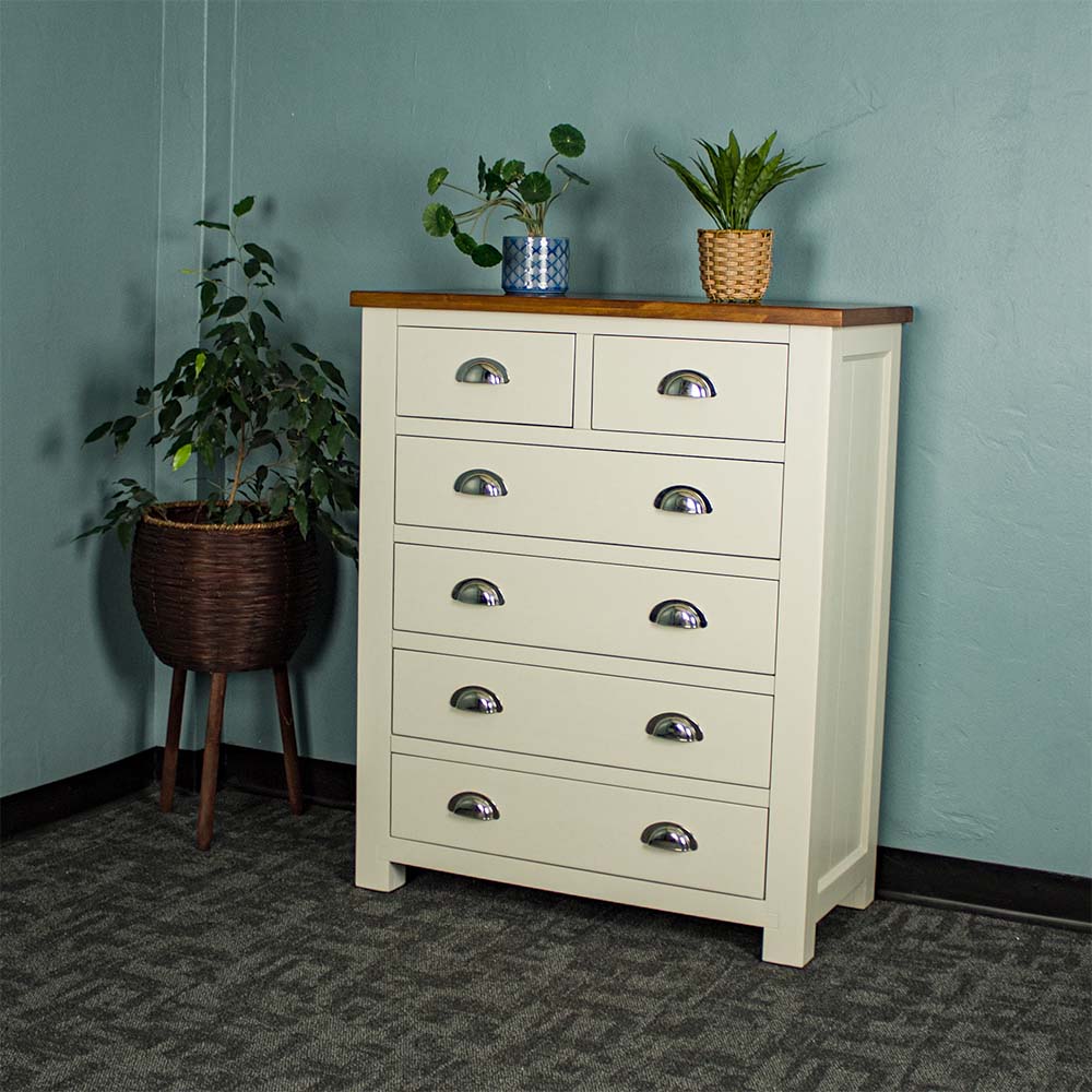 An overall view of the Alton 6 Drawer NZ Pine Tallboy. There is a free standing potted plant next to it. There are two potted plants on the top.