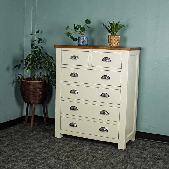 An overall view of the Alton 6 Drawer NZ Pine Tallboy. There is a free standing potted plant next to it. There are two potted plants on the top.