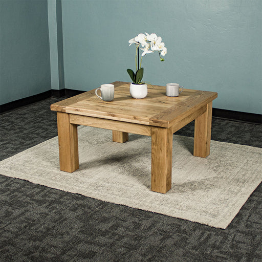 The front of the Amstel Square Oak Coffee Table. There is a pot of white flowers and two coffee mugs on top. The coffee table is on a white rug.