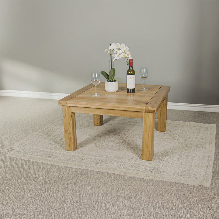 The front of the Amstel Square Oak Coffee Table. There is a pot of white flowers and two coffee mugs on top. The coffee table is on a white rug.