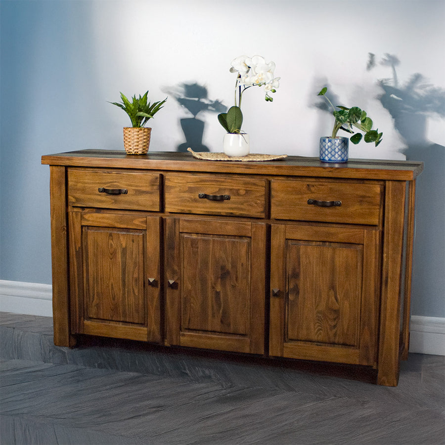 The front of the Botanica 3-Drawer Large Buffet. There are three potted plants on top, with the middle one on top of a rattan leaf.