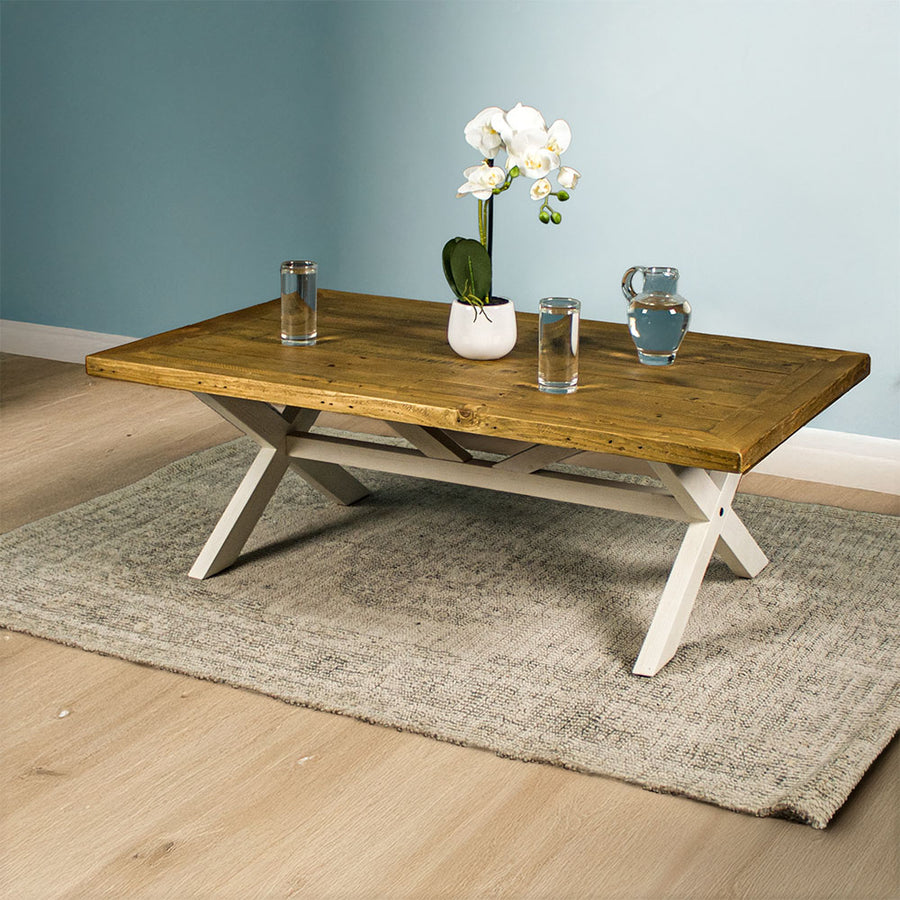 Front view of the Byron Recycled Pine Coffee Table. There are two glasses of water and a pitcher of water on top, as well as a small pot of white flowers.