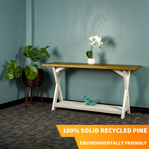 Front view of the Byron Recycled Pine Console Table. There is a standing potted plant next to it, a potted flower on top and two blue glass ornaments on the lower shelf.