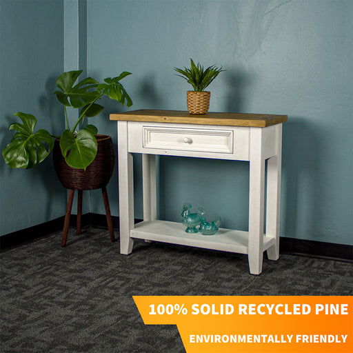 Front view of the Byron Recycled Pine Hall Table. There is a standing potted plant to the side, a small potted plant on top and two blue glass ornaments on the lower shelf.