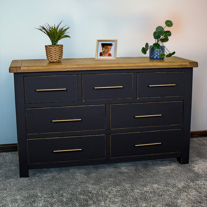 The front of the Cascais Oak Top 7 Drawer Lowboy (Black). There are two blue glass ornaments on top in the middle and two potted plants on either side.