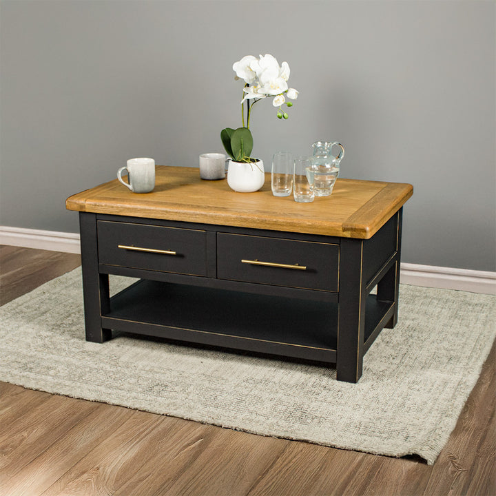 The front of the Cascais 2 Drawer Coffee Table. There is a pot of white flowers on top, two coffee mugs, a pitcher of water and two glasses on top.