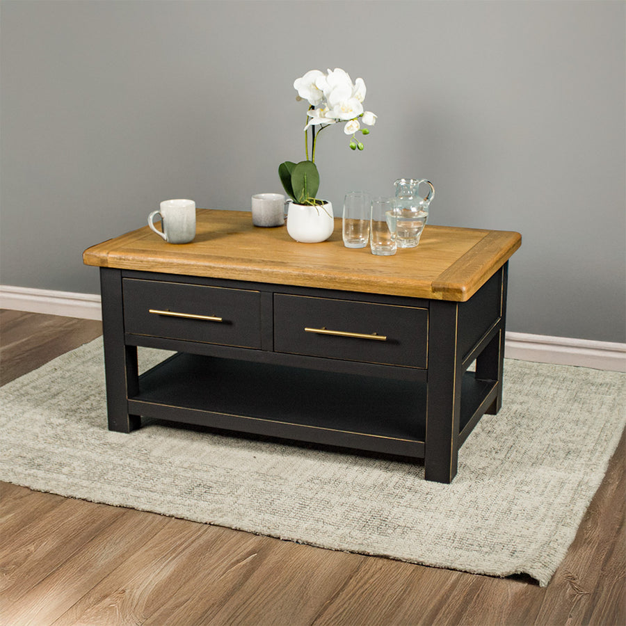 The front of the Cascais 2 Drawer Coffee Table. There is a pot of white flowers on top, two coffee mugs, a pitcher of water and two glasses on top.