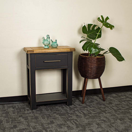 An overall view of the Cascais Black Hall Table. There are two blue glass ornaments on top and a free standing potted plant next to it.