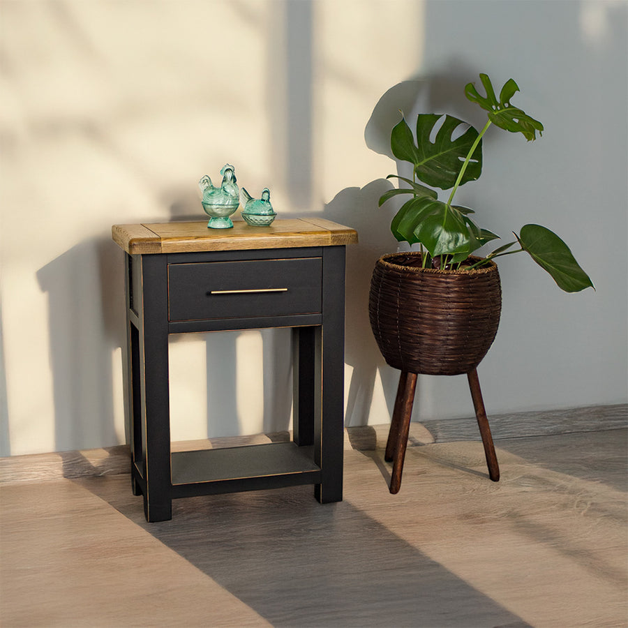 An overall view of the Cascais Black Hall Table. There are two blue glass ornaments on top and a free standing potted plant next to it.