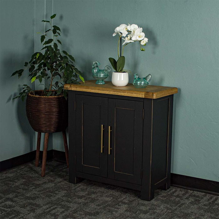 The front of the Cascais Oak-Top Small Sideboard. There are two blue glass ornaments on top with a pot of white flowers in between. There is a free standing potted plant next to the buffet.