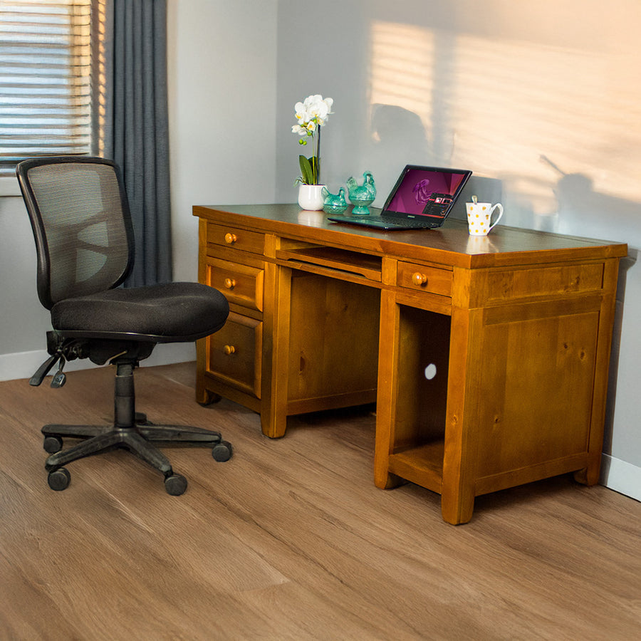 The front of the Cranford Computer Desk with Rimu Finish. There is an office chair in front. There is a small pot of white flowers, two blue glass ornaments, a laptop and a white coffee mug on top.