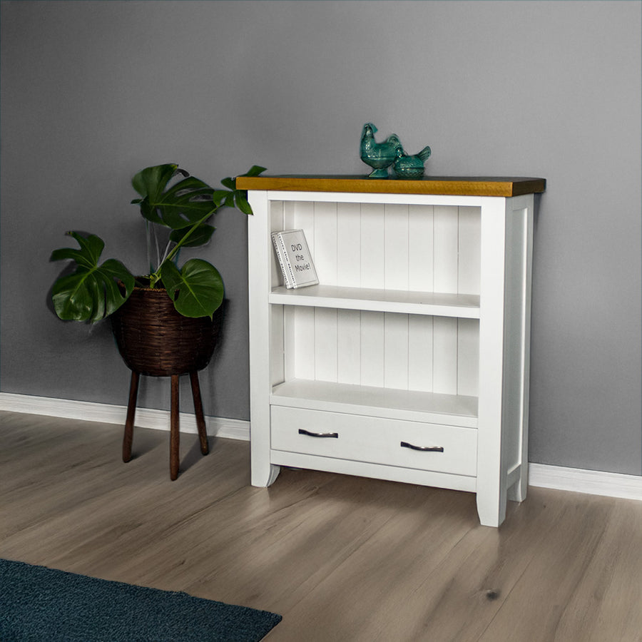 The front of the Felixstowe 1m Bookcase. There are two DVDs on the top shelf, and two blue glass ornaments on top of the bookcase. There is a free standing potted plant next to the bookcase.