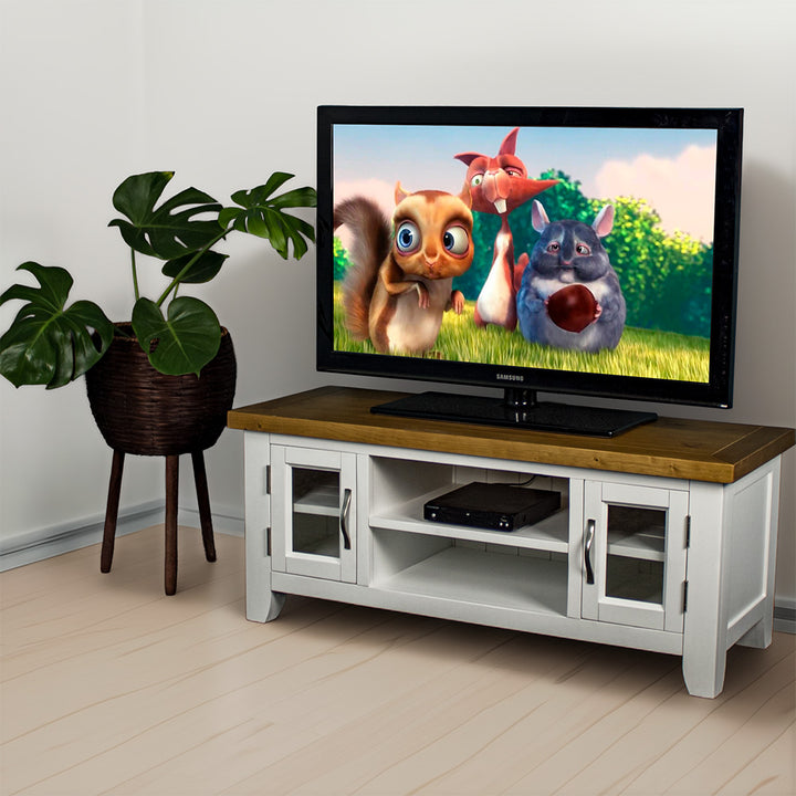 The front of the Felixstowe 2 Door Entertainment Unit (White). There is a DVD player in the top shelf in the middle and a large TV on top. There is a free standing potted plant next to the TV Unit.