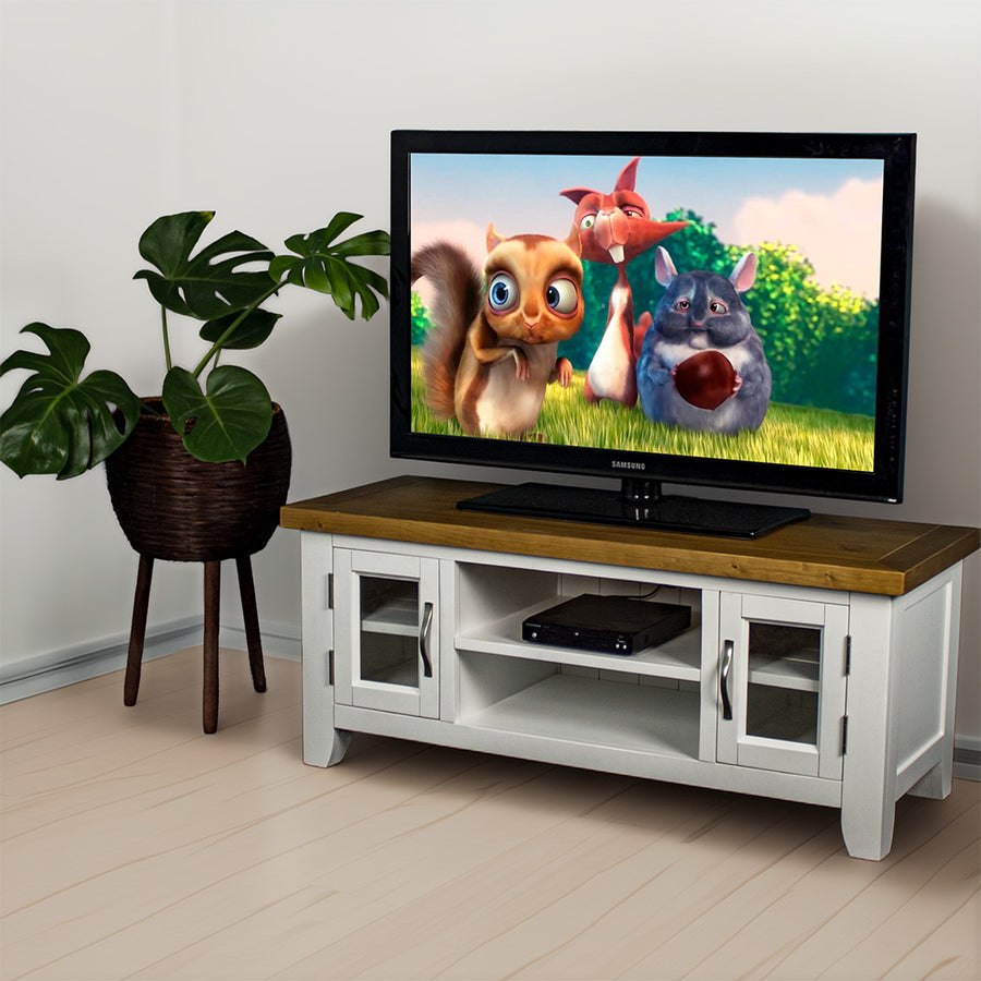 The front of the Felixstowe 2 Door Entertainment Unit (White). There is a DVD player in the top shelf in the middle and a large TV on top. There is a free standing potted plant next to the TV Unit.