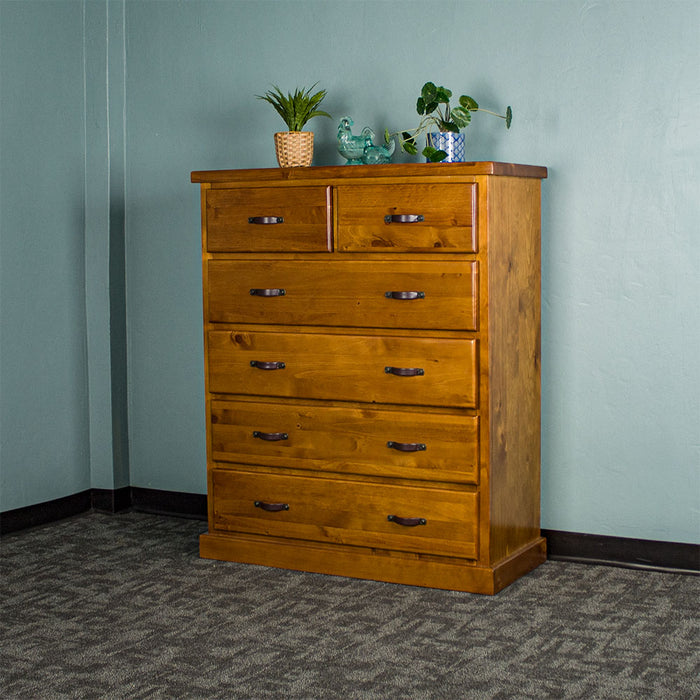 Front view of the Jamaica 6 Drawer Pine Tallboy. There are two potted plants on top and two blue glass ornaments.